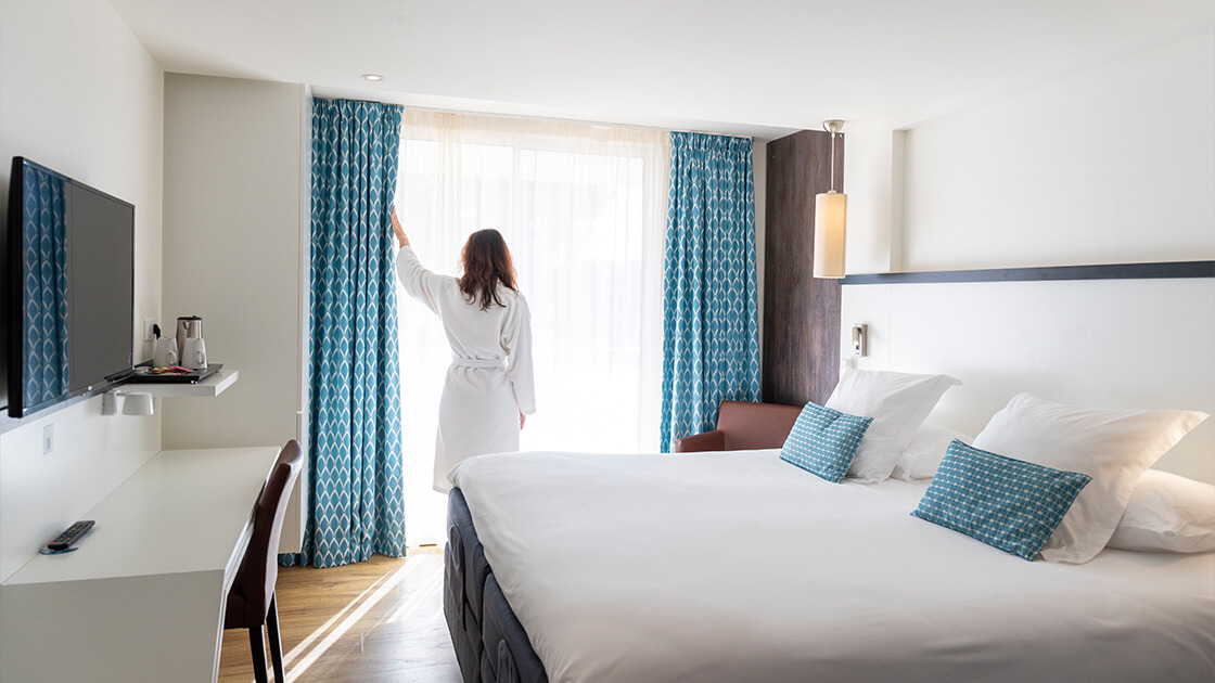 Chambre d’hôtel moderne avec grand lit, bureau et lumière naturelle.