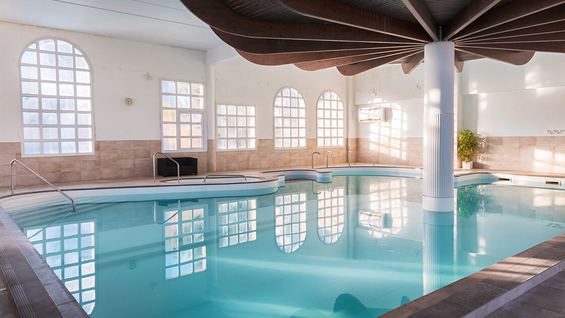 Piscine intérieure lumineuse avec grandes fenêtres et ambiance relaxante.